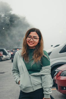 A smiling woman stands outdoors in foggy Tagaytay, Philippines, surrounded by parked cars.