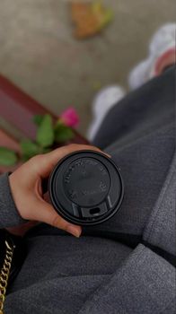 Hand holding a takeaway coffee cup outdoors with blurred urban background.