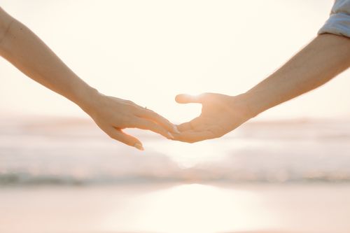 Free Romantic moment of hands reaching towards each other against a sunset beach backdrop. Stock Photo