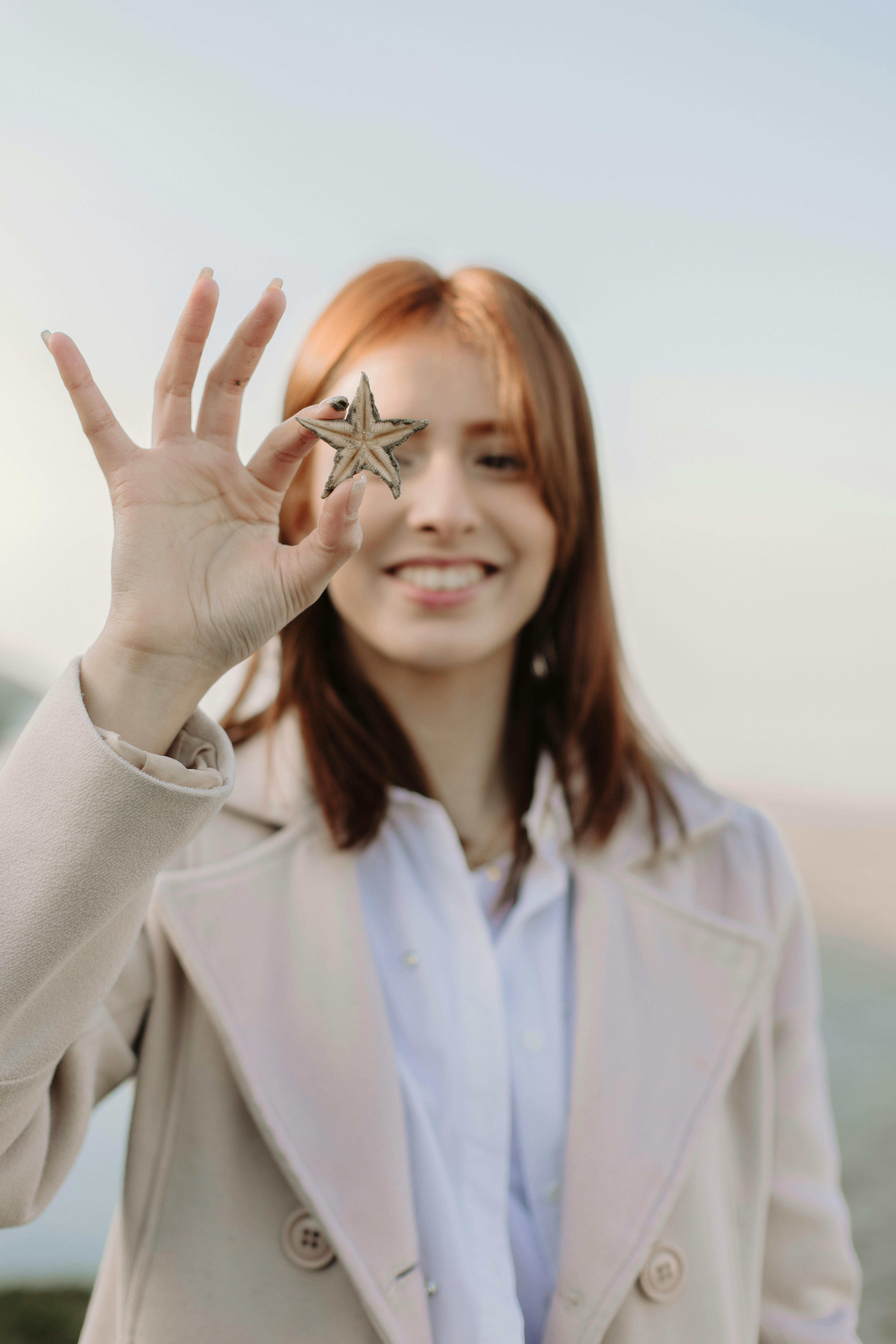 Miễn phí Người phụ nữ trẻ mỉm cười cầm một con sao biển, tượng trưng cho sự khám phá và thiên nhiên. Ảnh lưu trữ