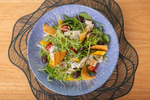 A vibrant Mediterranean salad featuring mixed greens, tomatoes, olives, and tortilla chips in a blue bowl.