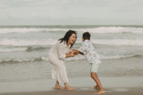 Free A mother and son share a joyful moment playing on a sandy beach by the ocean. Stock Photo