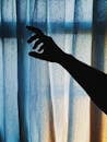 剪影的手伸向柔和的窗帘，在室内营造出戏剧性而阴郁的氛围