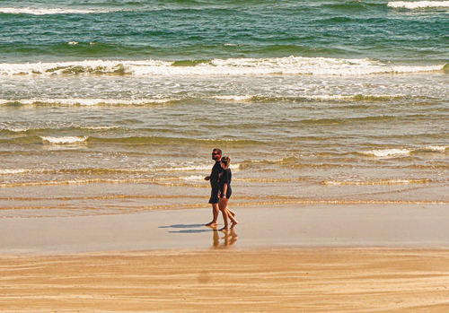 Free A couple enjoying a peaceful walk along a sunny beach with gentle waves. Stock Photo