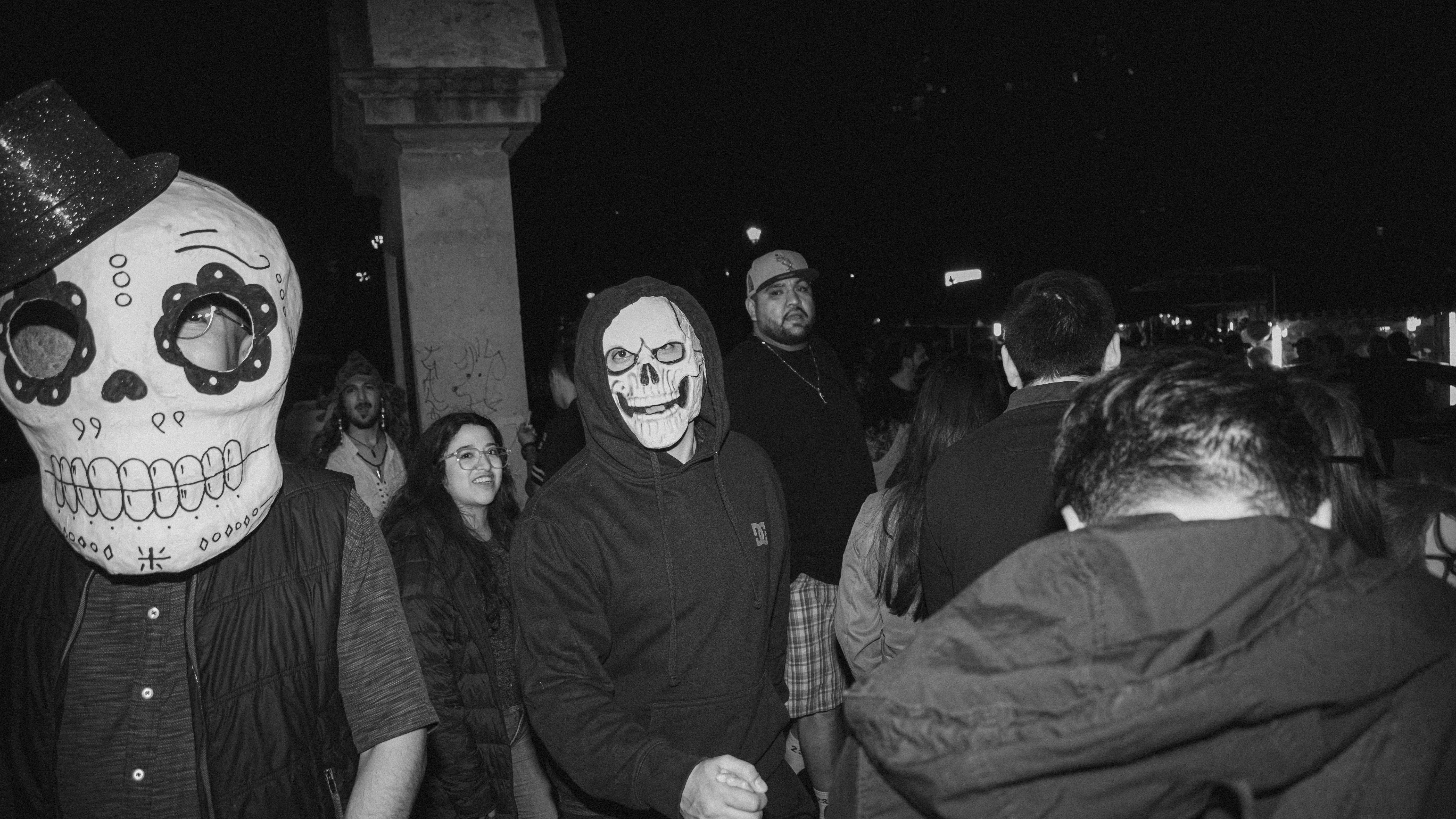 Black and white photo of a Halloween celebration with people in spooky costumes and masks at night.