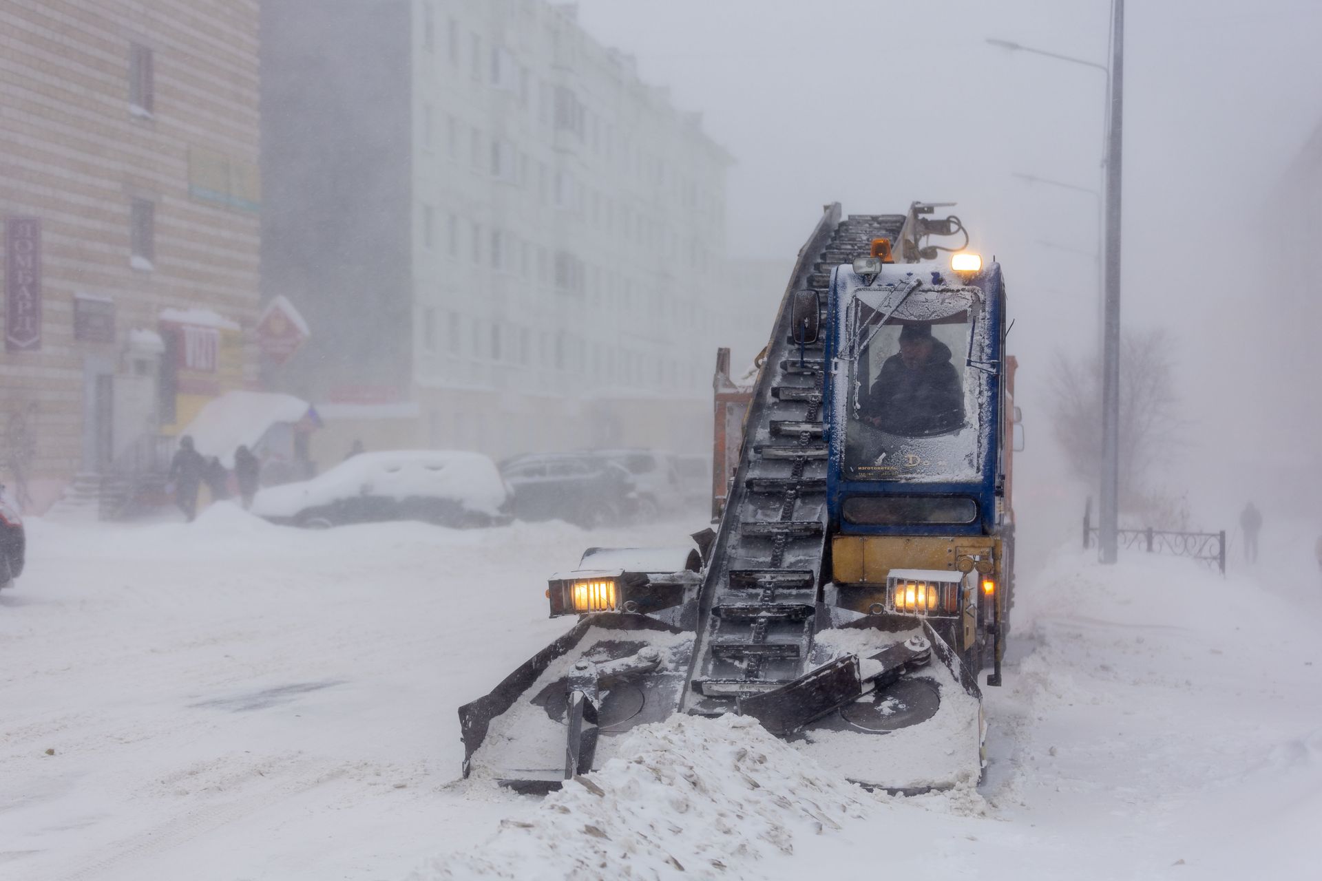 Snow-covered street in city with snow plow clearing heavy snowfall, creating a wintery urban scene.
