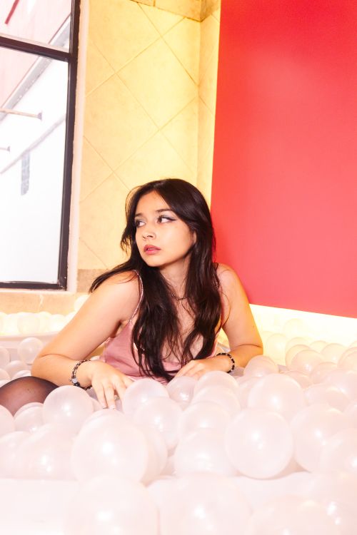 Free A young woman sits in a ball pit surrounded by soft white balls and a vibrant red background. Stock Photo