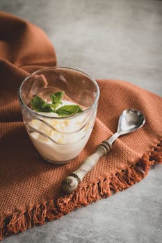 A refreshing glass of creamy dessert topped with mint leaves on a rustic cloth with a vintage spoon.