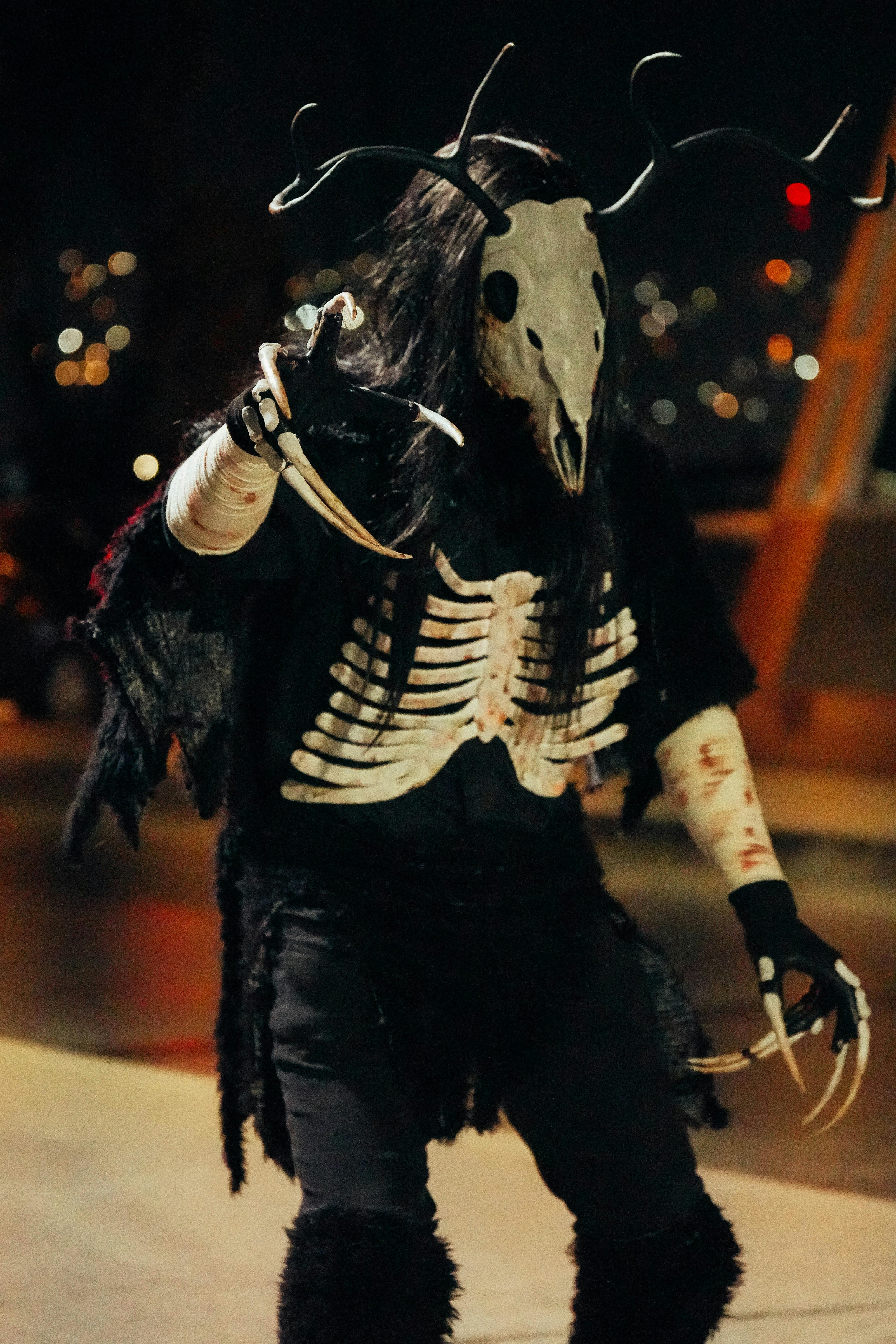 grátis Uma pessoa vestida como uma criatura mística com um esqueleto e uma máscara de chifre em um ambiente noturno. Foto profissional
