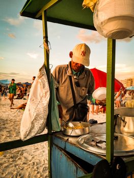 A beach vendor serving food at sunset on a bustling beach, capturing a warm vacation scene.