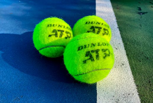 Vivid close-up of three Dunlop ATP tennis balls on a colorful outdoor court.