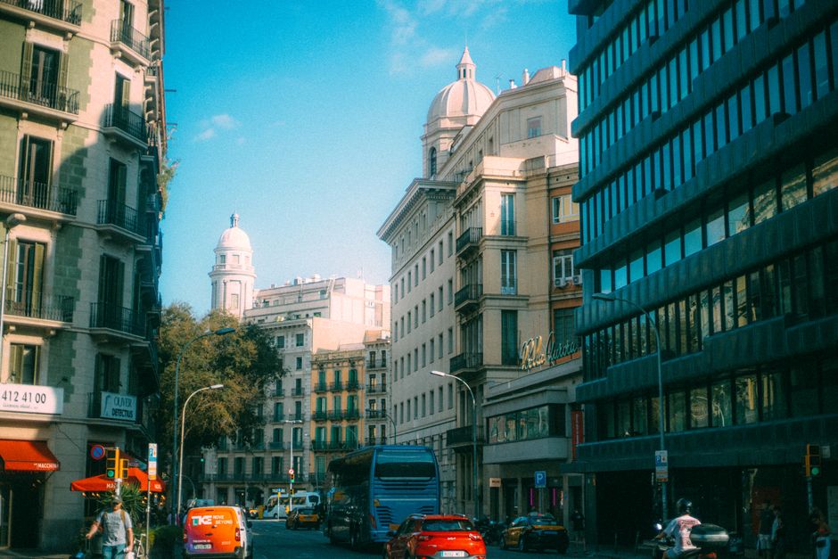 Calle concurrida de la ciudad con edificios históricos y tráfico bajo un cielo azul claro.
