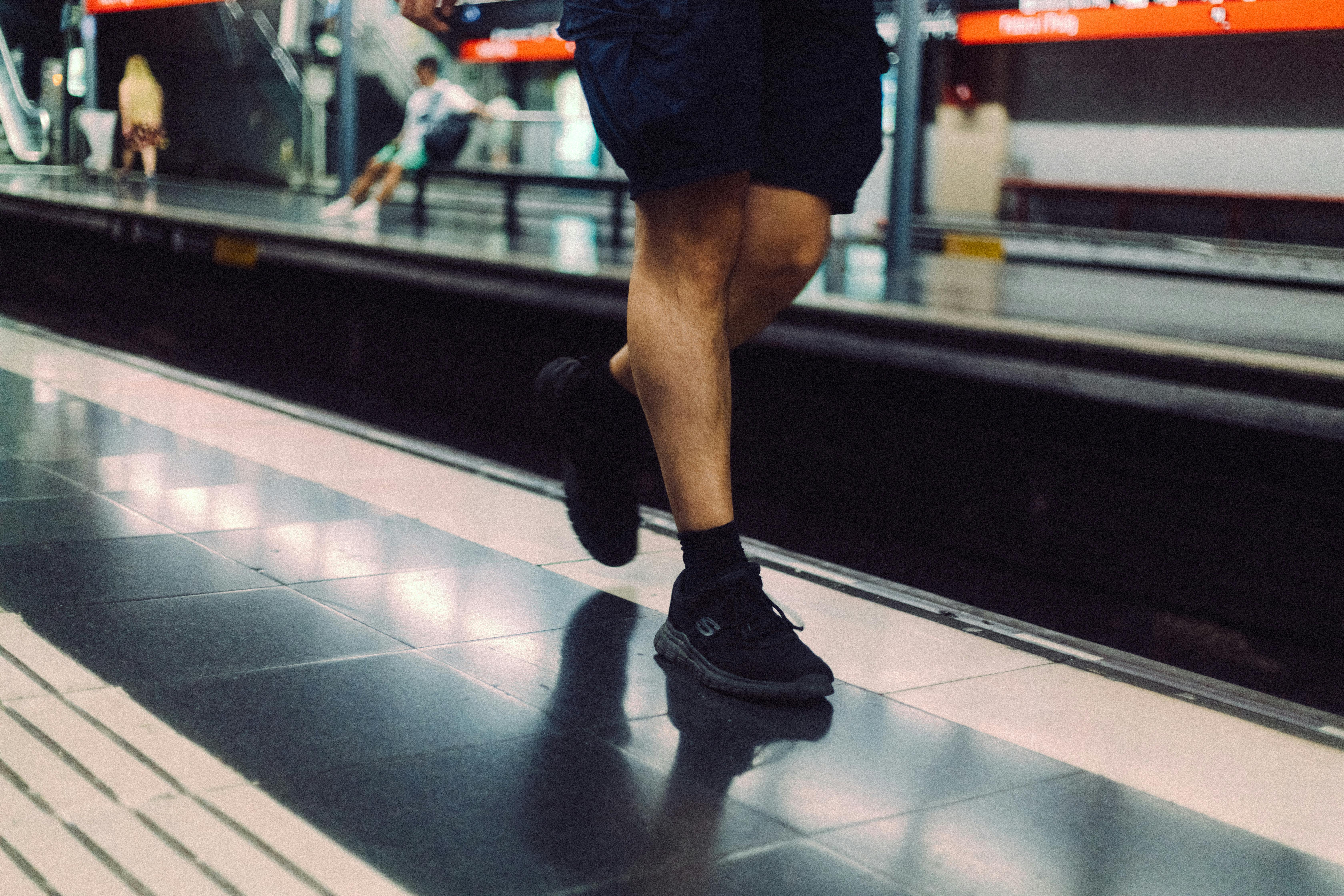 De franc Cames d'home amb sabatilles esportives en una plataforma de metro, escena de trànsit urbà. Foto d'estoc