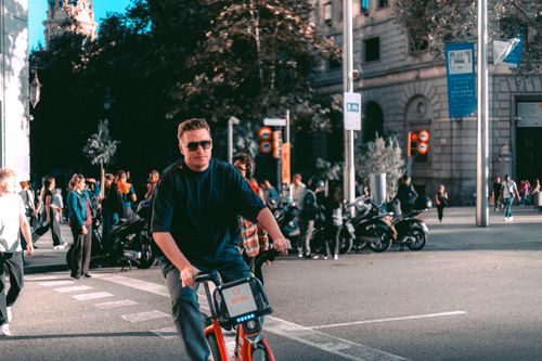 Free Man rides bike on city street during daytime, amidst bustling crowd. Stock Photo