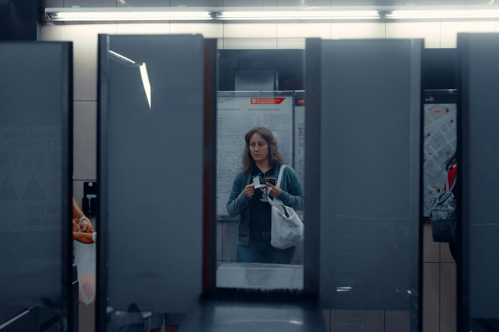 Woman holding a bag, standing in front of subway turnstiles, city map in background.