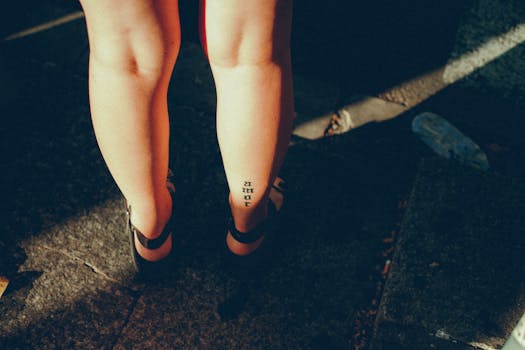 A woman's tattooed legs in sandals, highlighted by sunlight on a stone path.