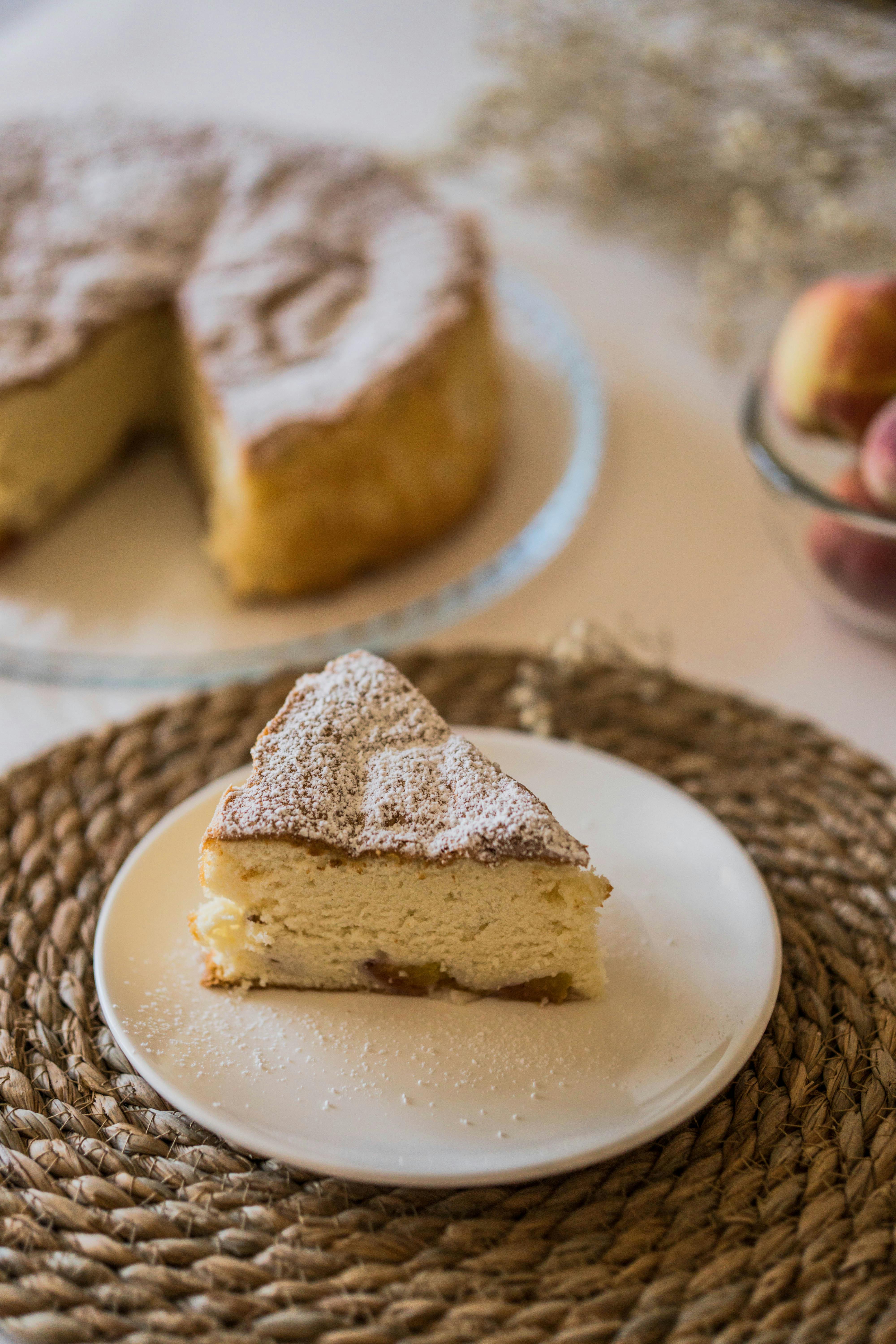 Slice of peach cake dusted with powdered sugar on a woven placemat.