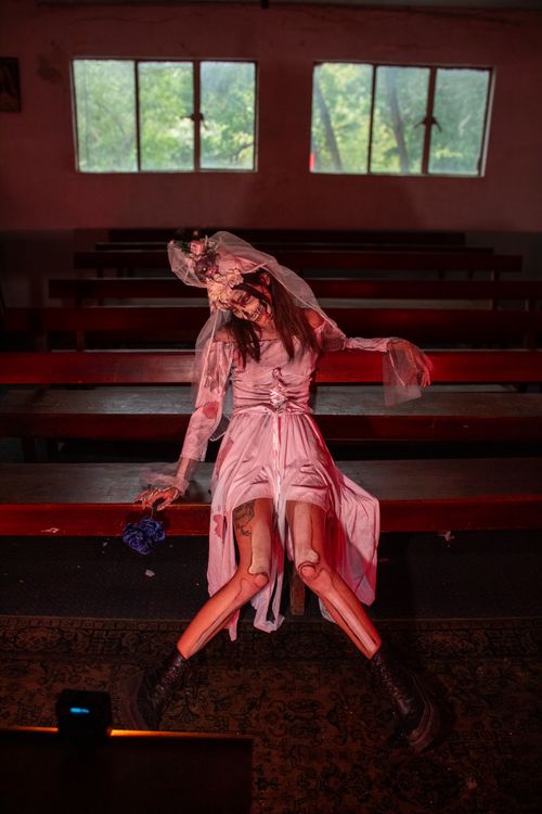 Free A creepy bride doll sits ominously on benches inside an abandoned building. Stock Photo