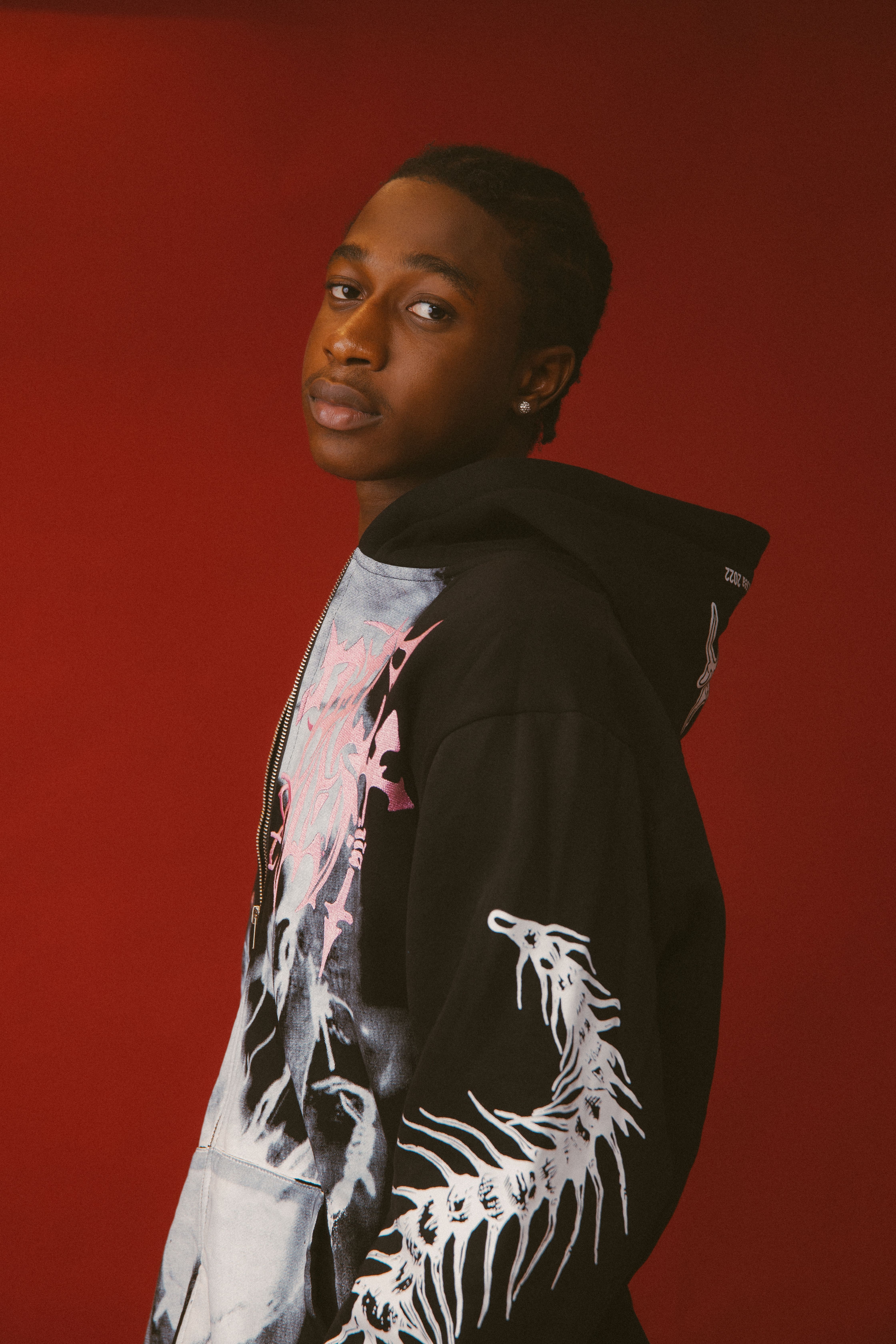 Young man in a trendy urban hoodie against a red background, capturing modern fashion style.
