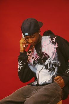 Casual young man in hoodie chatting on phone against vibrant red backdrop. Urban style concept.