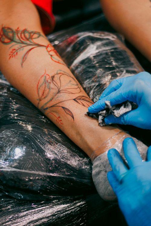 Free Artist adds final touches to a vibrant floral tattoo on forearm with glove-covered hands. Stock Photo