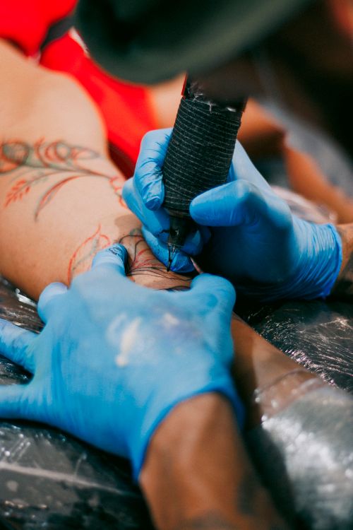 Free Skilled tattoo artist working on a colorful body ink design on a client's arm using tattoo machine in studio. Stock Photo
