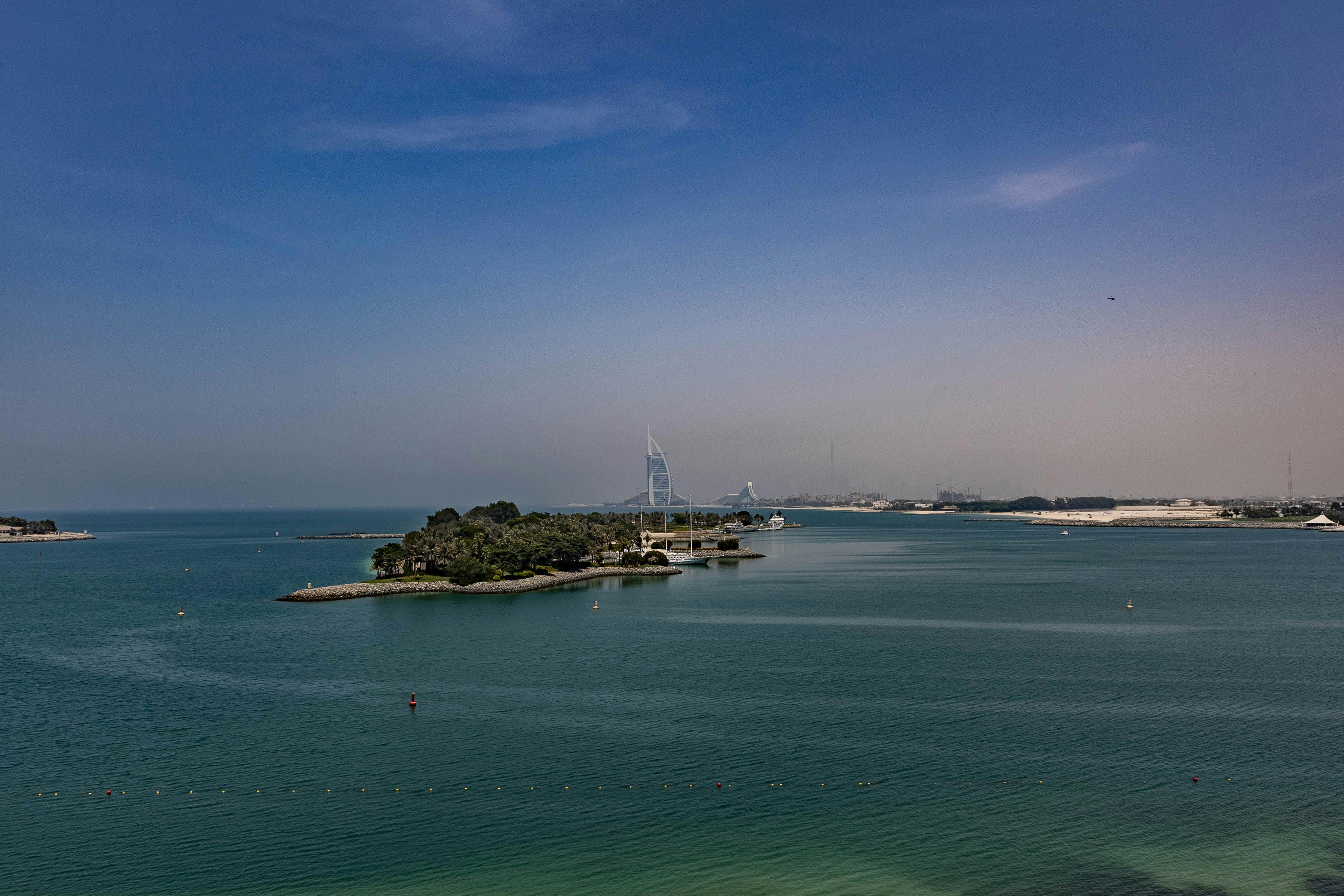 Aerial view of Dubai's coastline with Burj Al Arab in the distance under a clear blue sky.