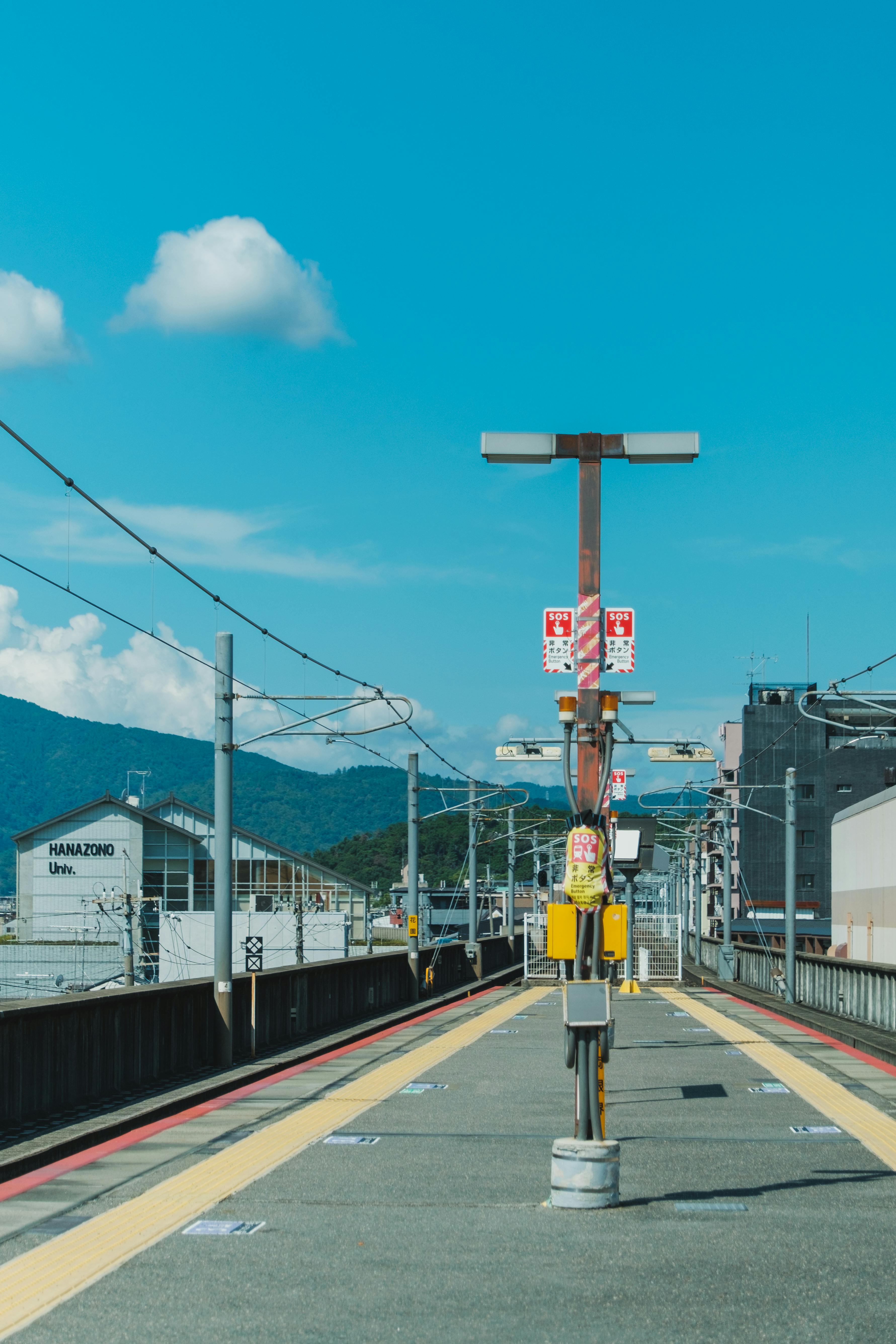 Deserted train platform under a clear sky at Hanazono Station, showcasing urban tranquility.