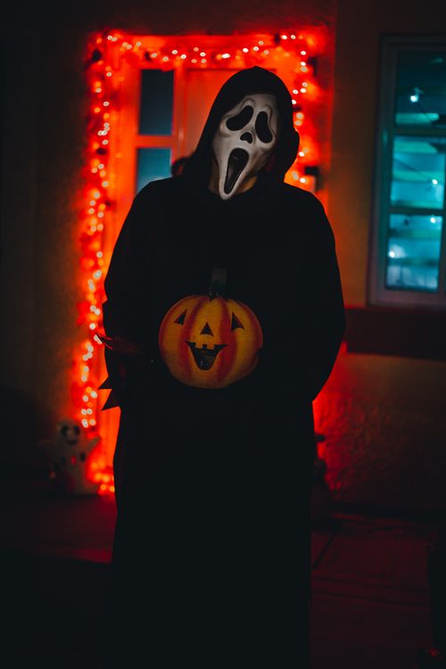 Free A person in a ghost mask holding a jack-o'-lantern in a Halloween-themed setting. Stock Photo