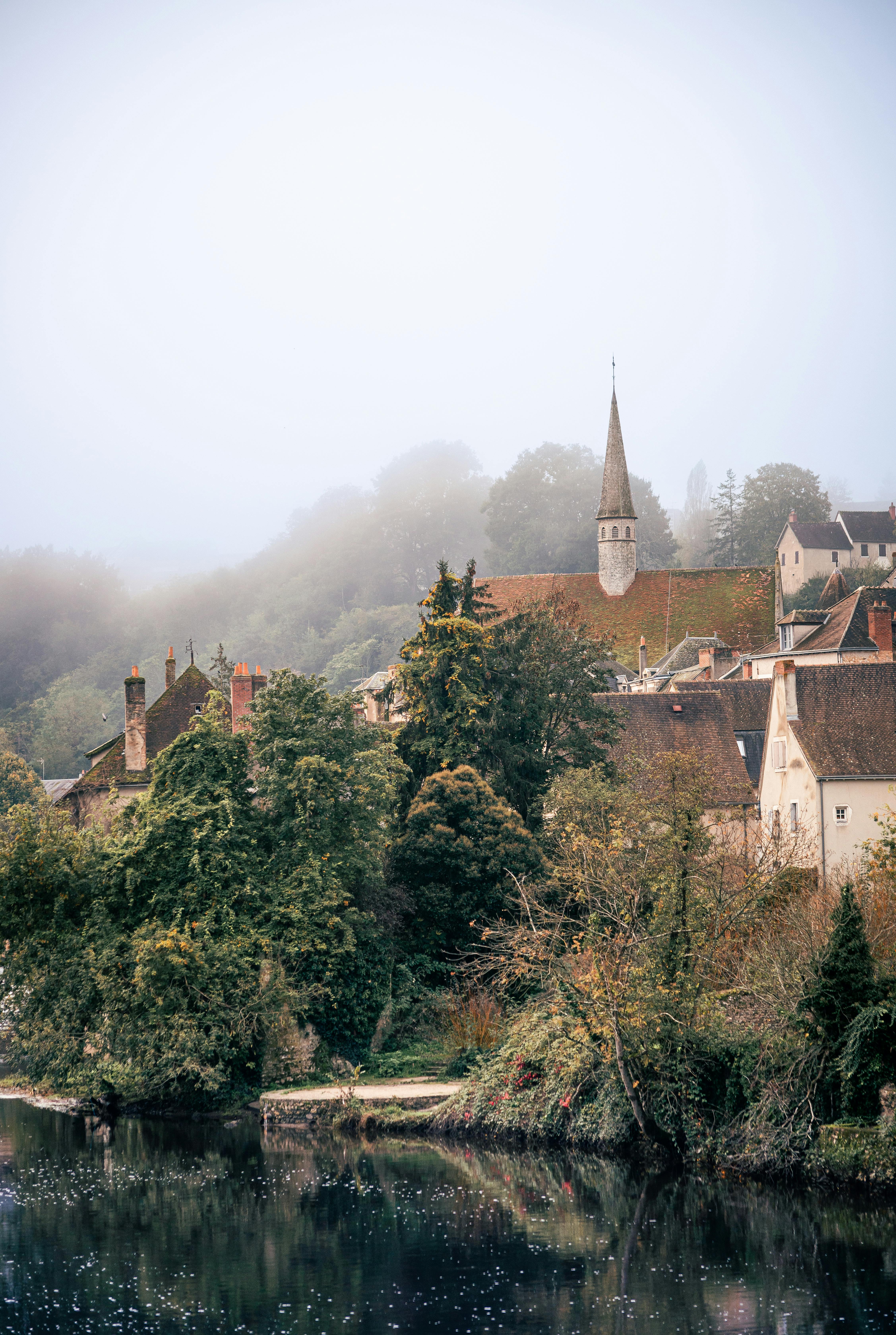 Quaint village scene with church spire and lush foliage in a foggy morning.
