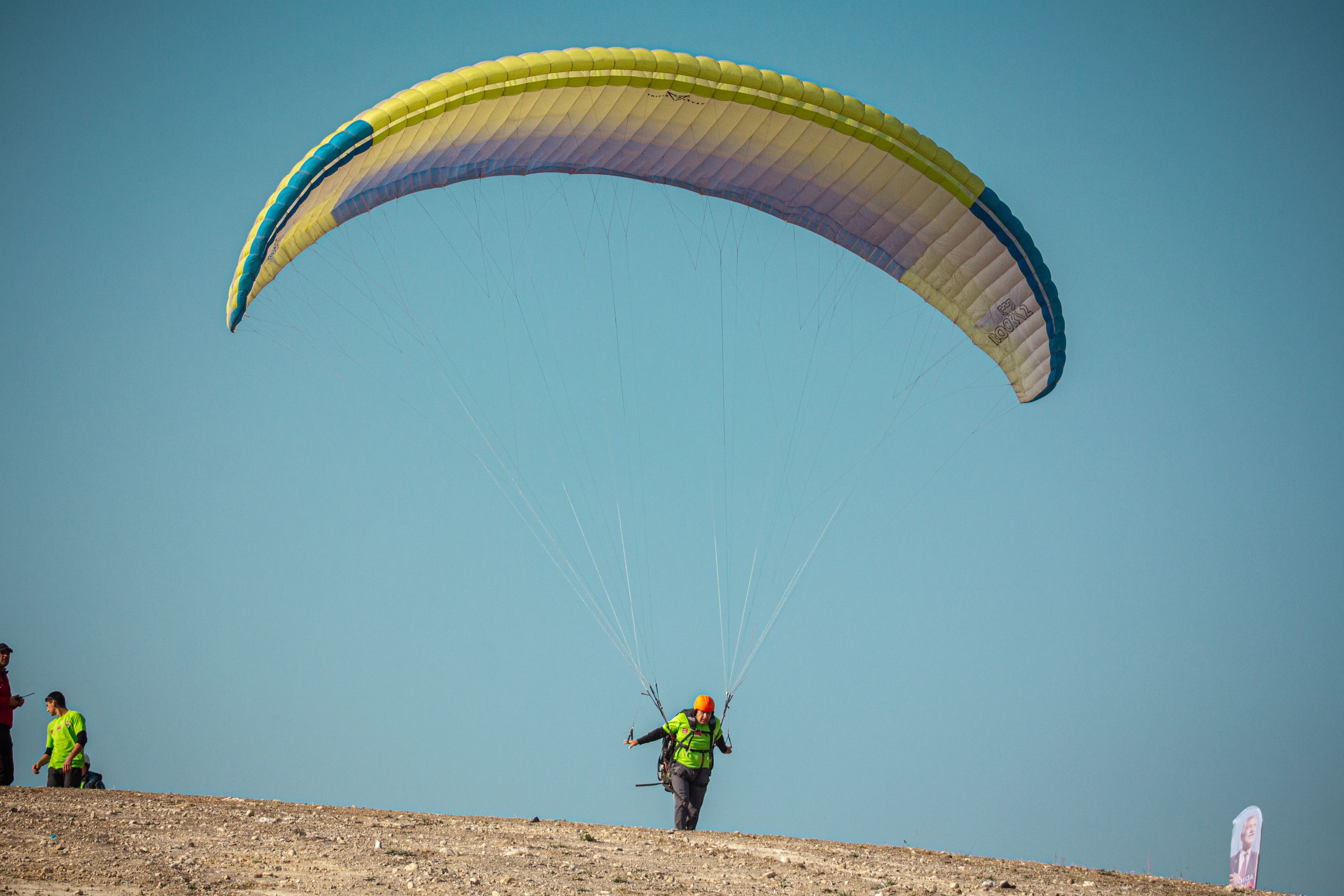 Parachutist landing on a dry landscape under a clear blue sky.
