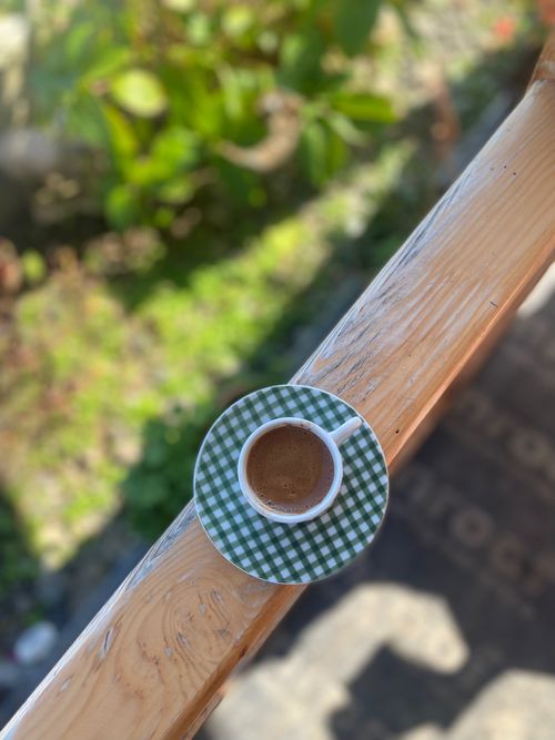 Free Aerial view of a coffee cup on a wooden balcony with greenery in the background. Stock Photo