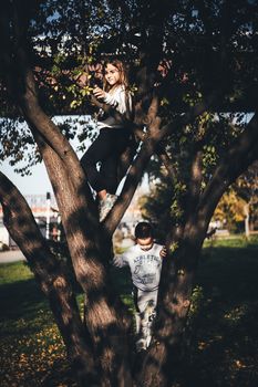Two children climbing a tree in a sunny autumn park, enjoying outdoor play.