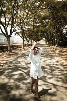 一位身穿白衣的年轻女子，白天在绿树成荫的小路上若有所思地摆着姿势