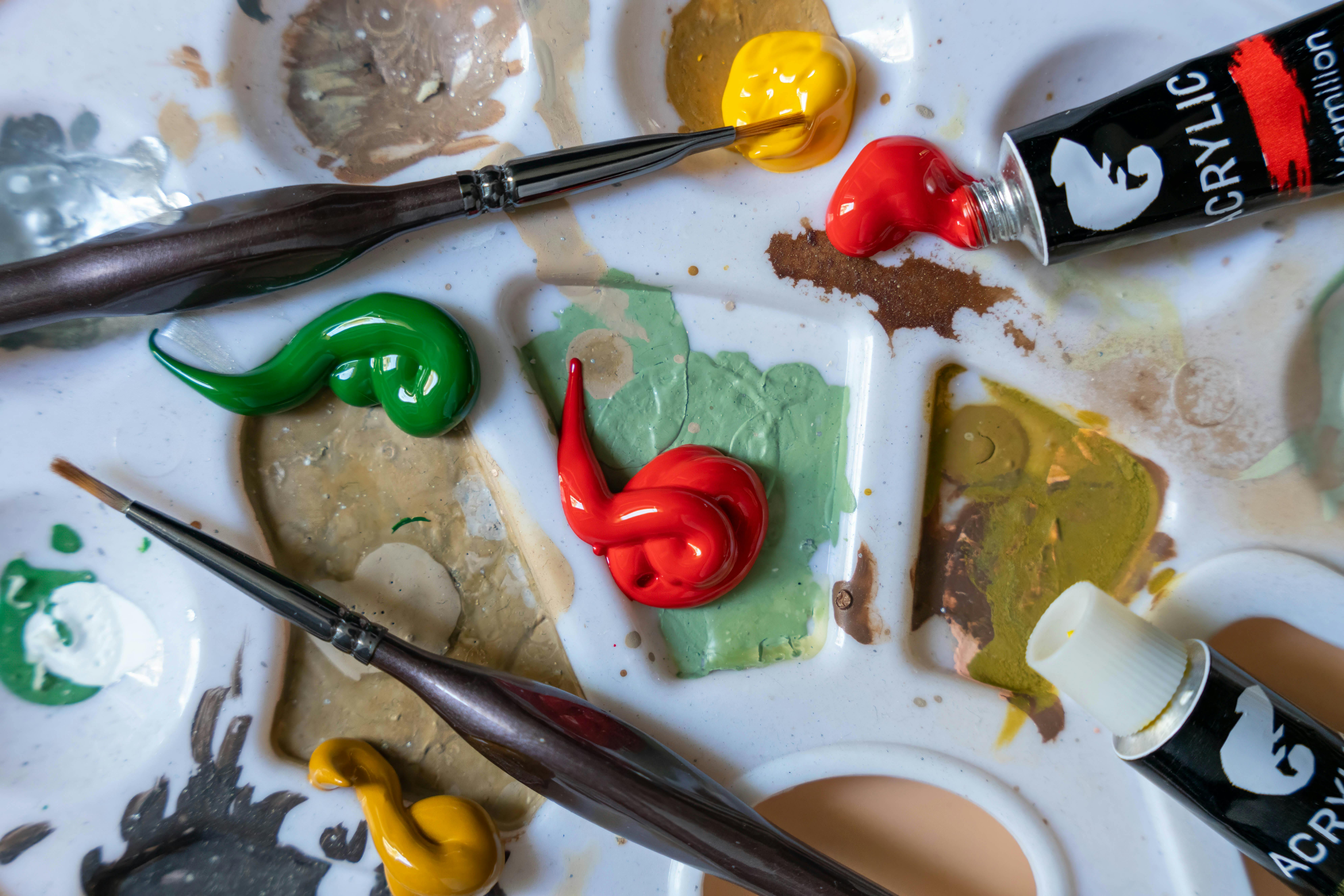 Close-up of vibrant acrylic paints and brushes on an artist's palette, creating a vivid artistic scene.