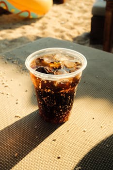 Refreshing iced cola drink on a sandy beach in Parga, Greece under a warm sun.