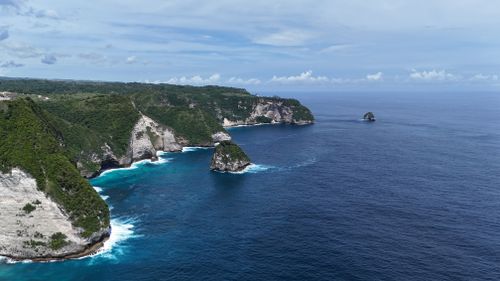 Free Stunning aerial photo of a rocky coastline with vibrant blue ocean and lush greenery. Stock Photo