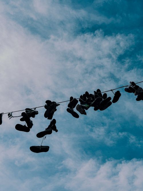 Free Artistic view of multiple shoes hanging on a wire against a bright blue sky with clouds. Stock Photo