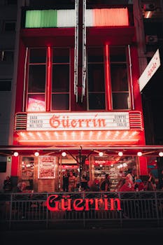 Colorful night scene at a bustling pizzeria with neon lights and outdoor seating.