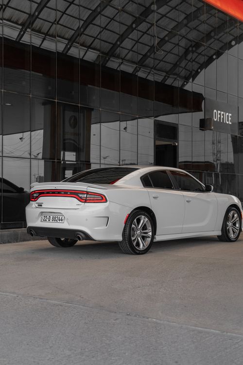 Free Modern white Dodge Charger parked outside a glass office building, showcasing sleek design. Stock Photo