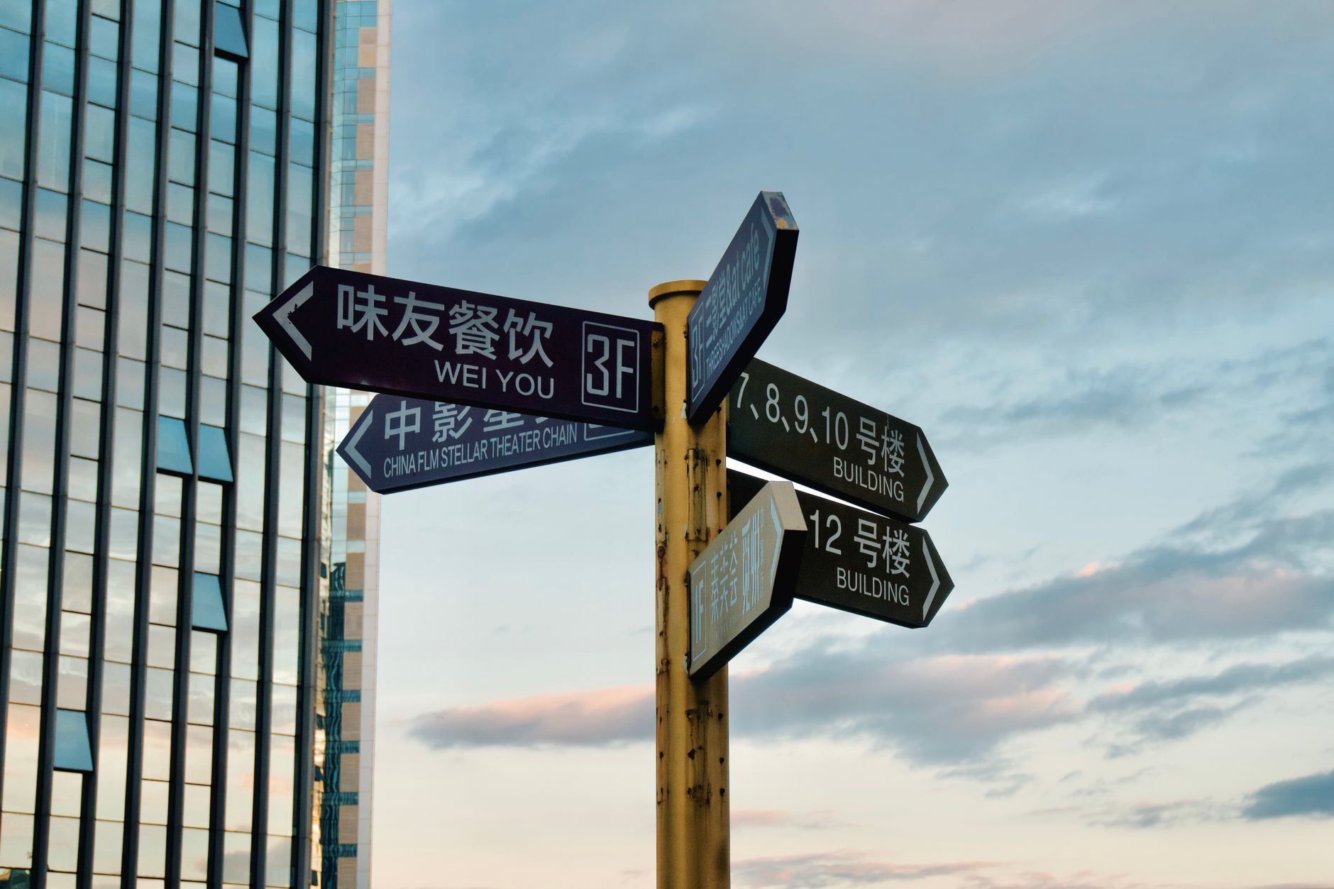 Direction signs in urban area with skyscraper backdrop at sunset.