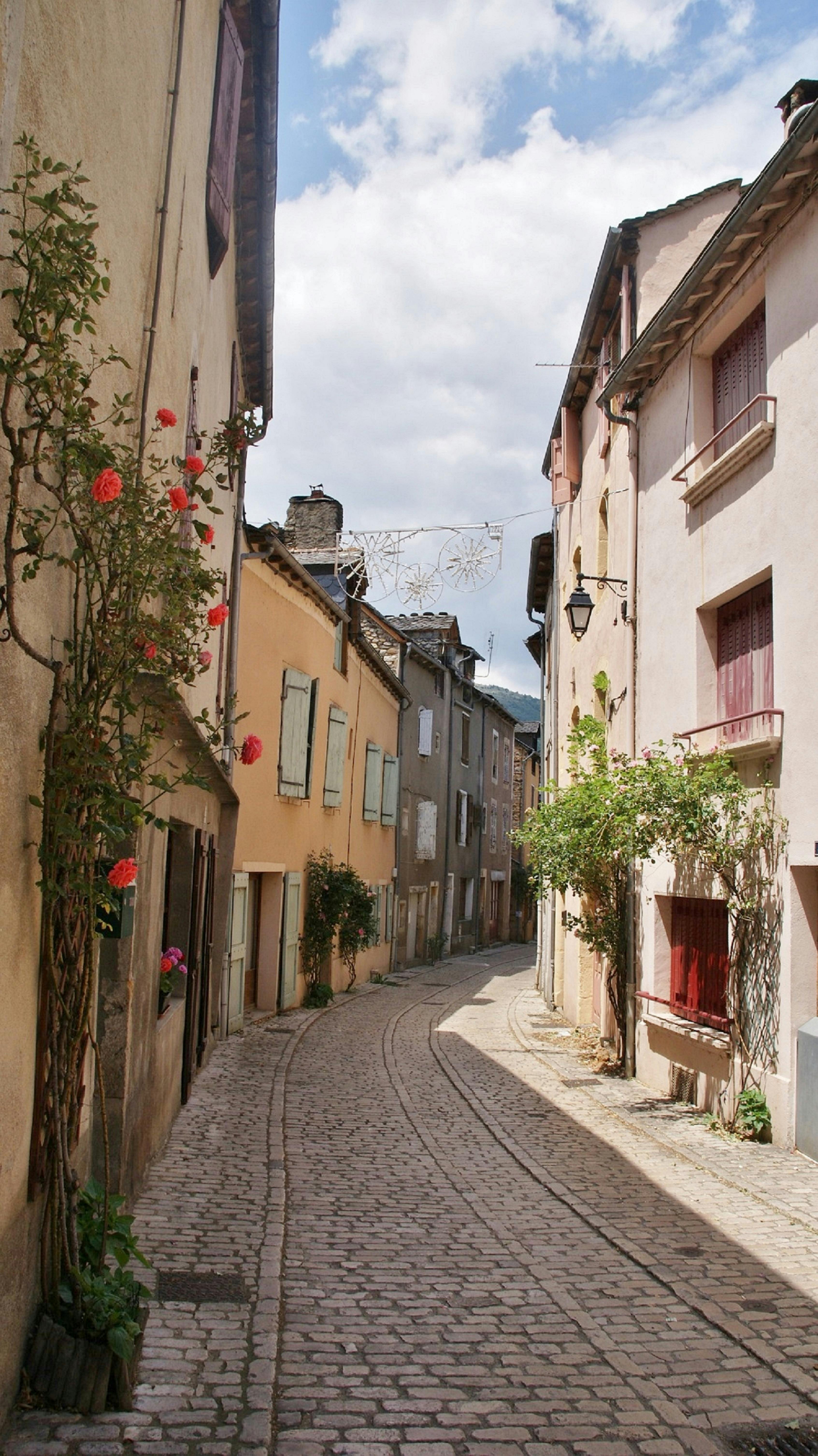 Idyllic cobblestone street in Ispagnac, France with charming houses under a blue sky.