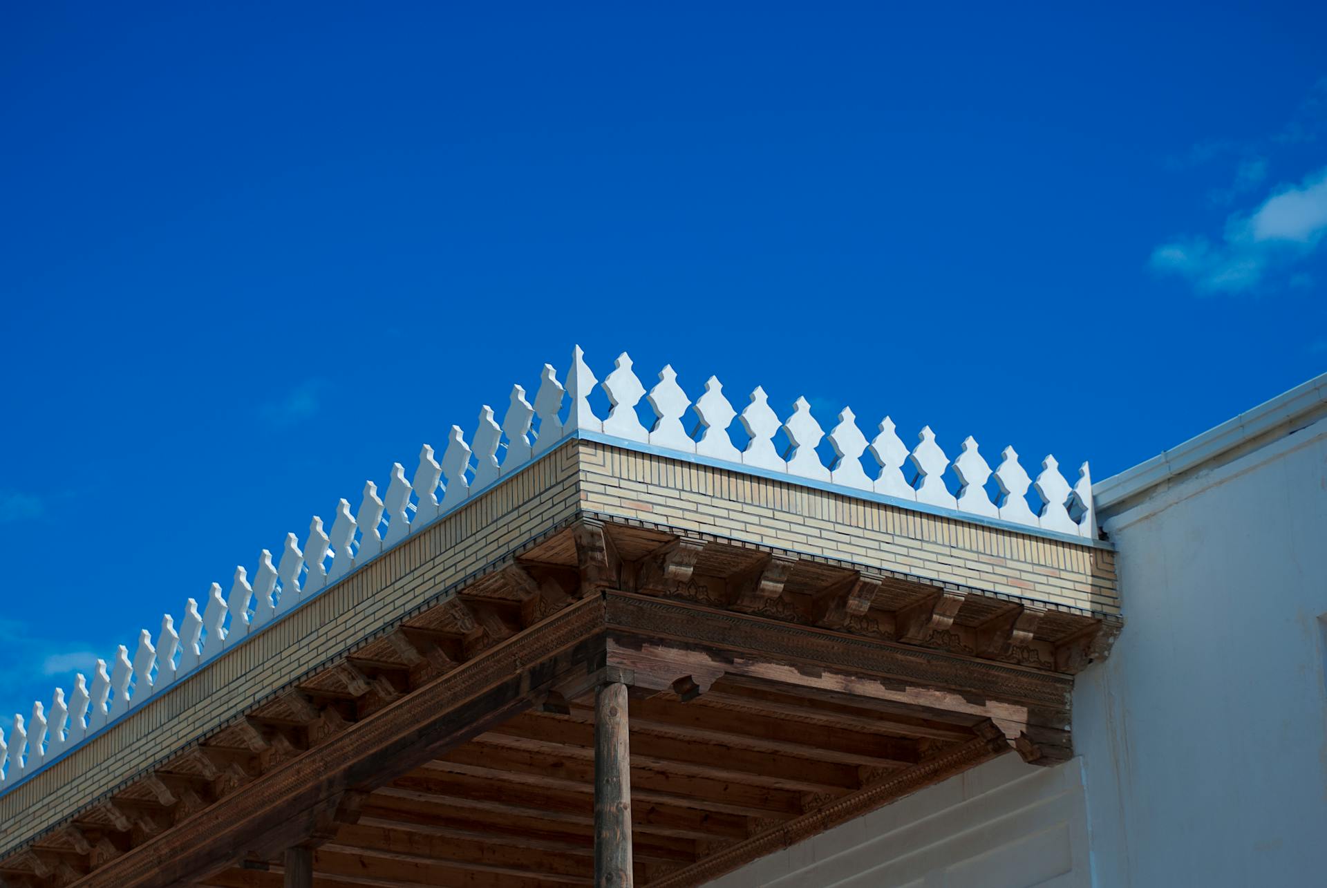 Close-up of decorative wooden roof with white trim against a vivid blue sky.