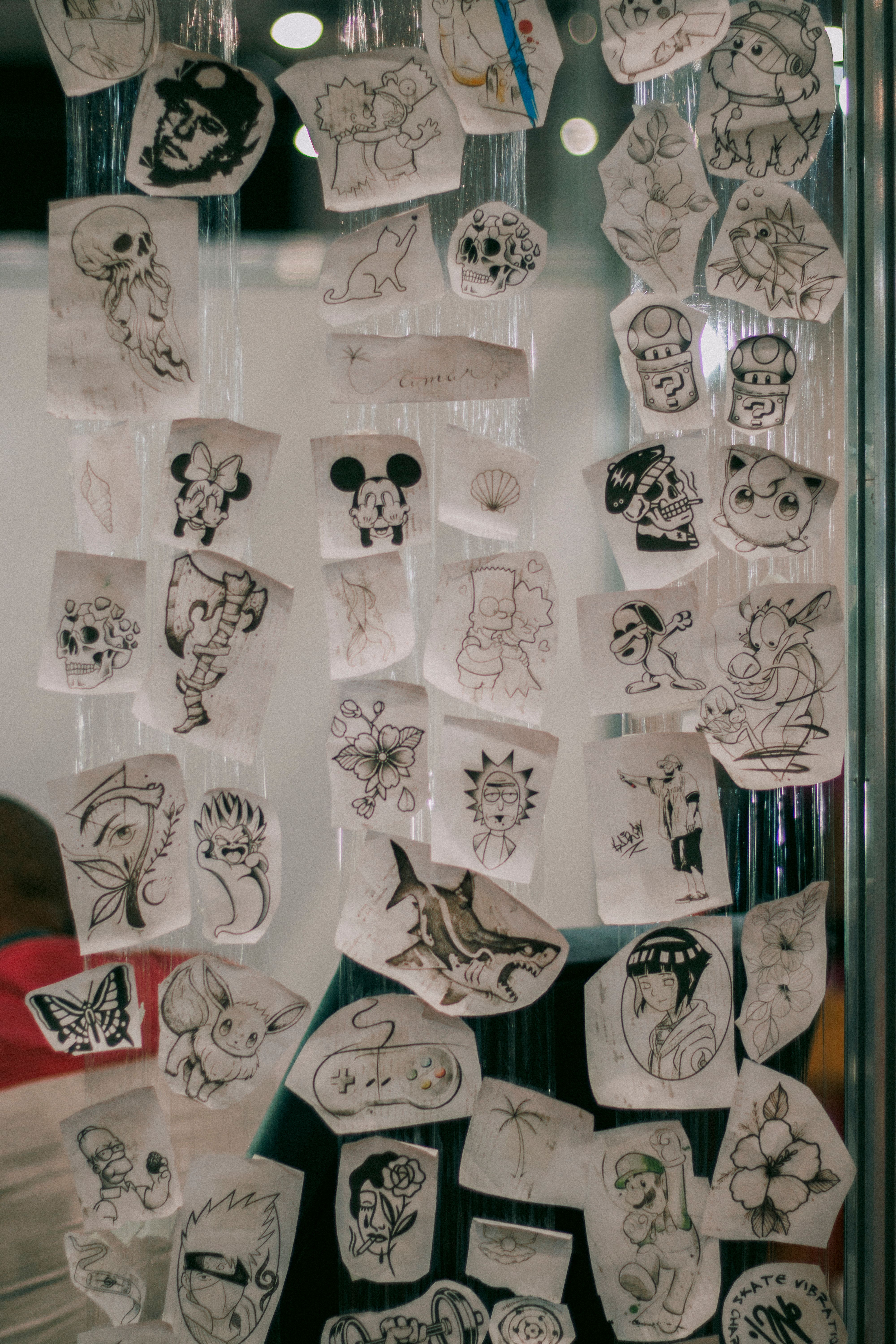 Collection of various monochrome hand-drawn tattoo illustrations on a glass surface
