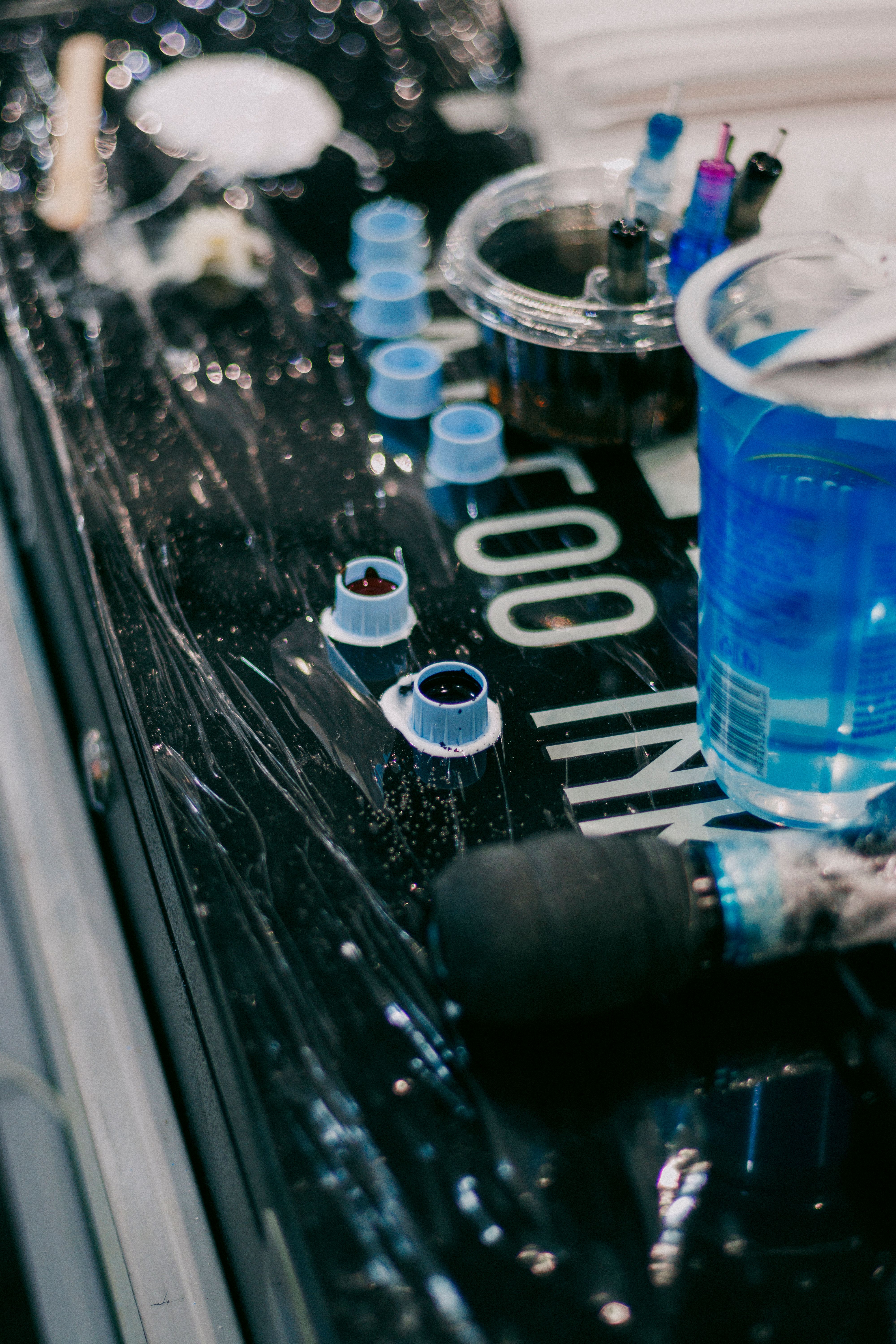 A close-up of tattooing supplies, including ink caps, cartridges, tools and a blue bottle arranged on a reflective work surface.