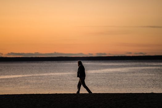 Person walking along Stamford shoreline at sunrise, casting a silhouette. Tranquil coastal scene.
