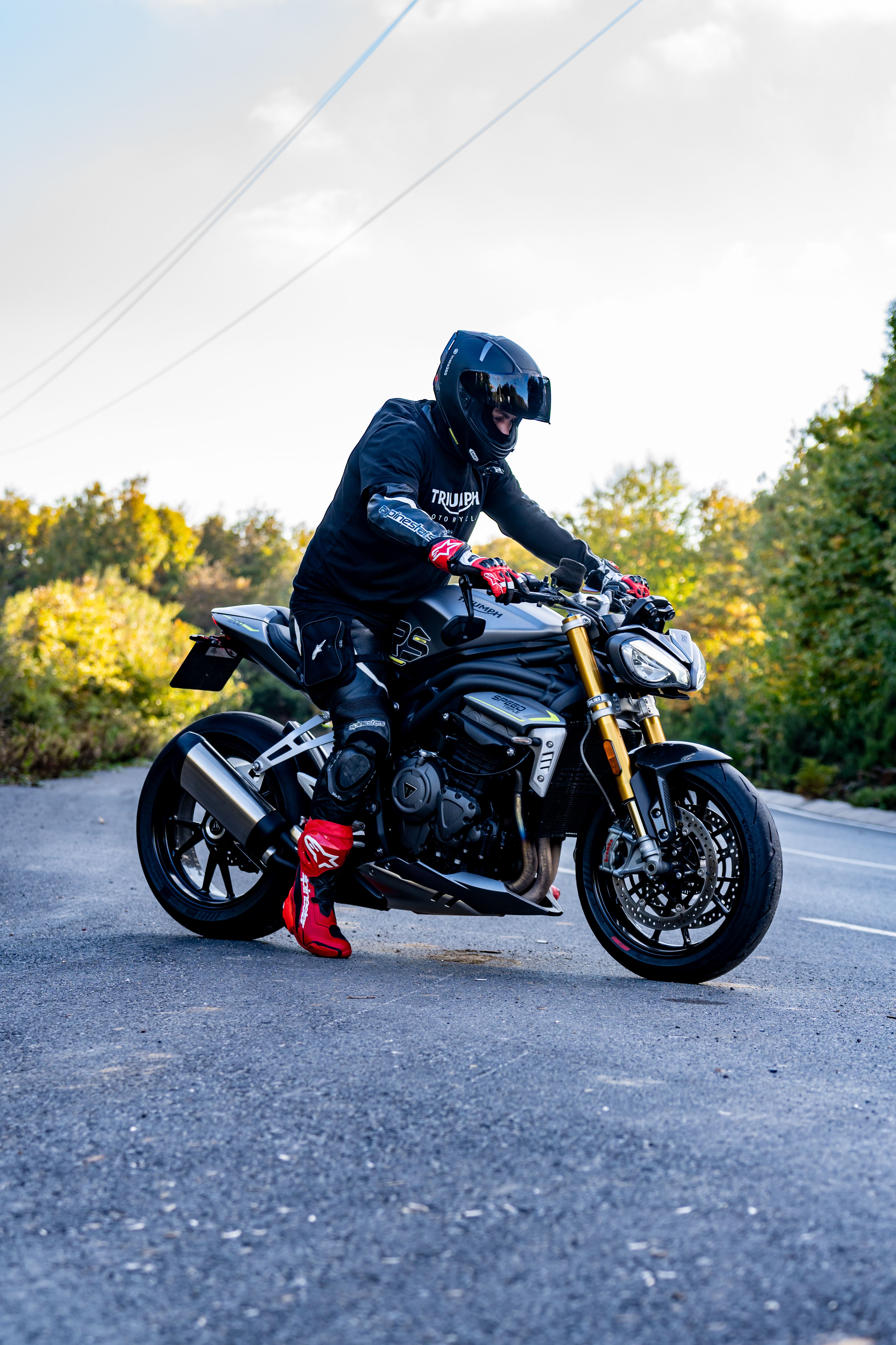 A motorcyclist in gear riding a Triumph bike on an open road, surrounded by nature.