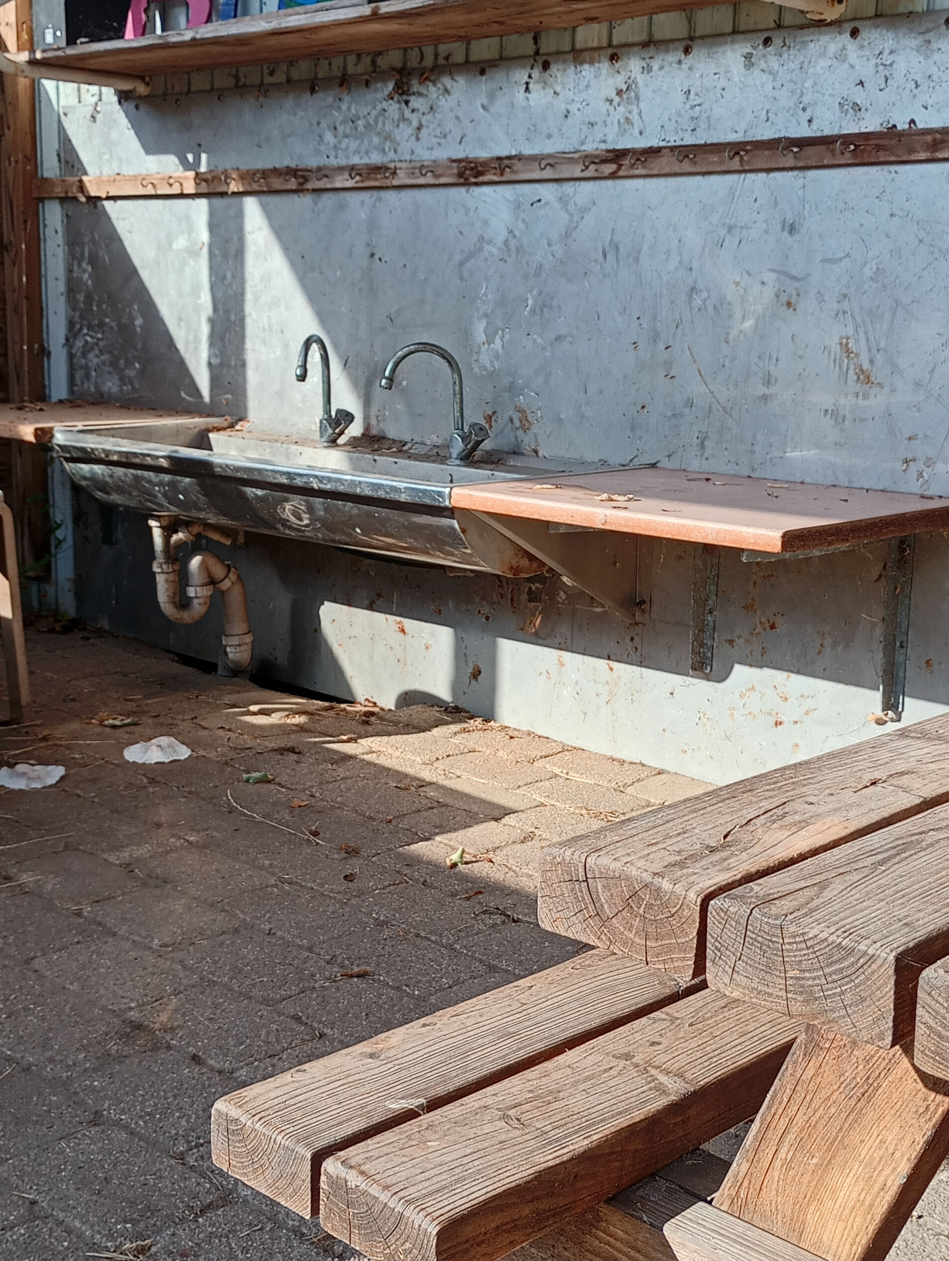 An outdoor industrial-style sink with wooden benches in natural light.