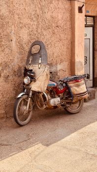 A vintage motorcycle against a textured wall in Iran, capturing local charm.