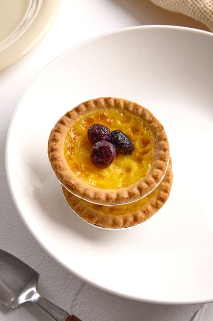 Mouthwatering custard tart topped with fresh berries on a white plate.